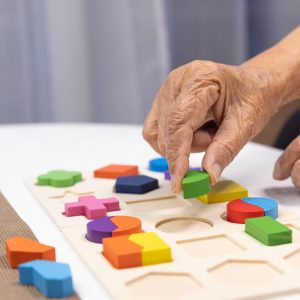 caregiver-and-senior-woman-playing-wooden-shape-puzzles-game-for-dementia-prevention